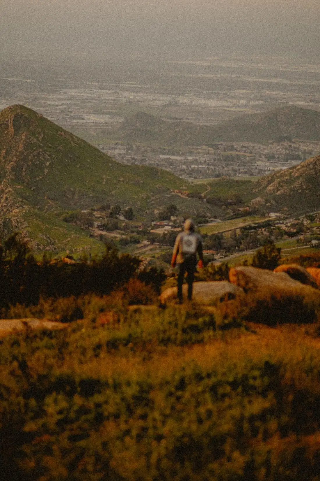 A hiker looking down at a valley from a rocky slope at sunset