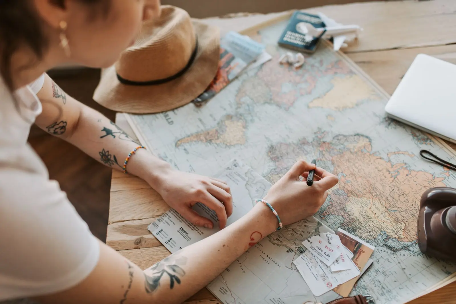 Hands marking a route on a paper map beside a sun hat