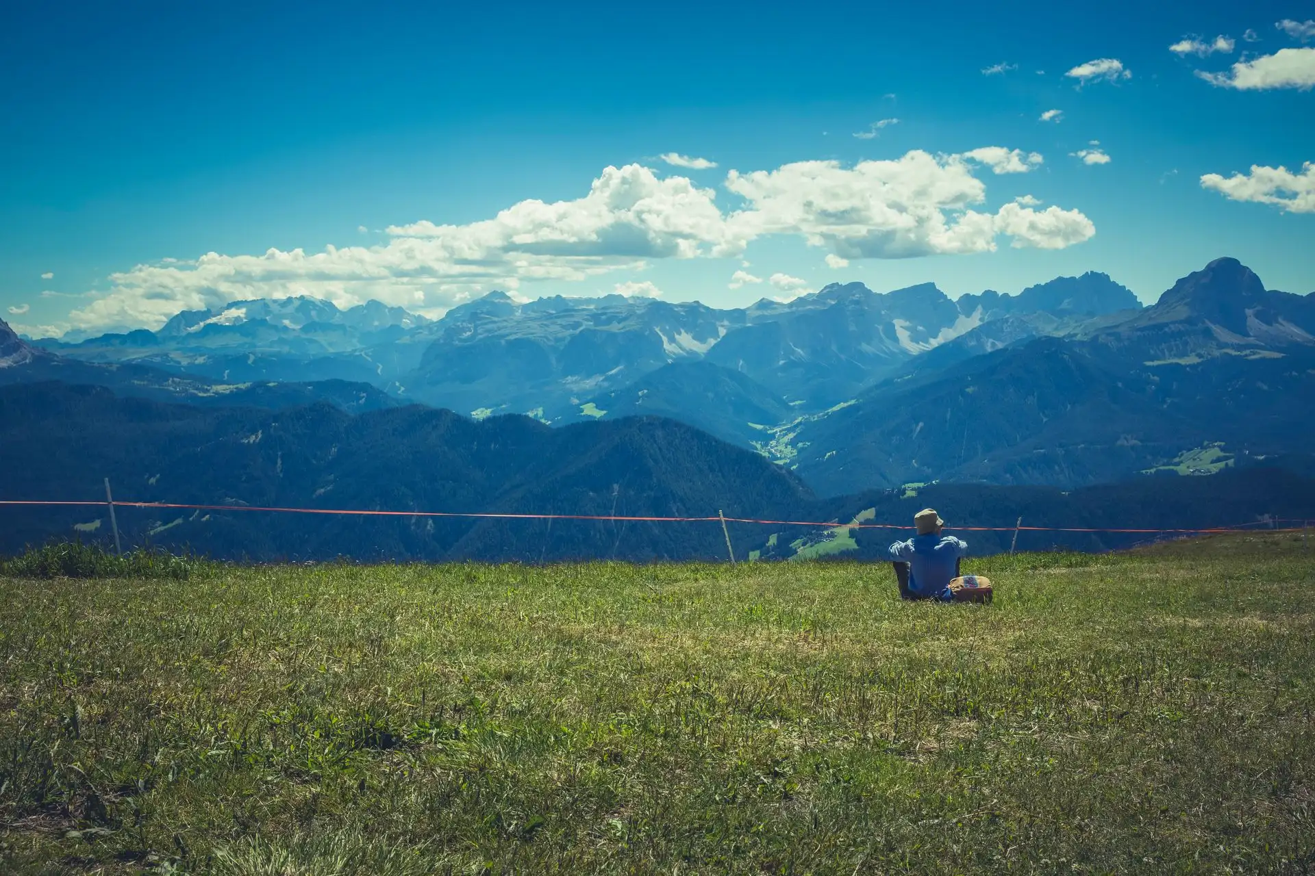 A traveller sitting on a grassy ridge above a mountain valley